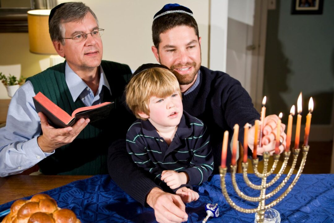 Bambino di quattro anni con il nonno e il padre che illuminano la menorah di Hanukkah