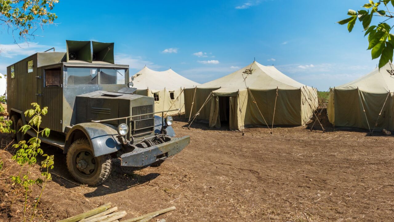 Retro german World War II military truck Krupp L3H163 is standing near a row of old canvas tents in a military camp.