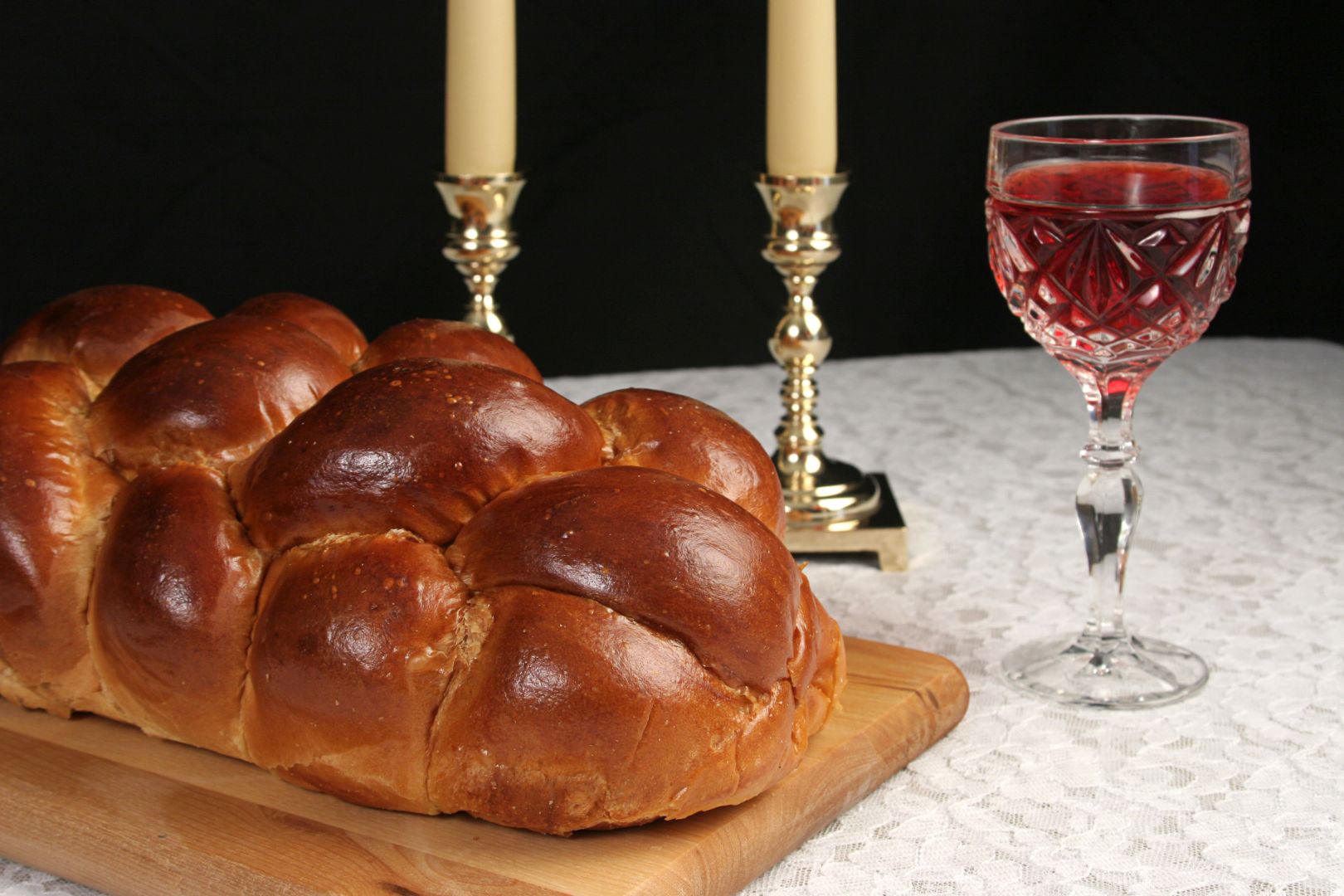 A table set for Shabbat with challah bread, candlesticks and wine. Black background.