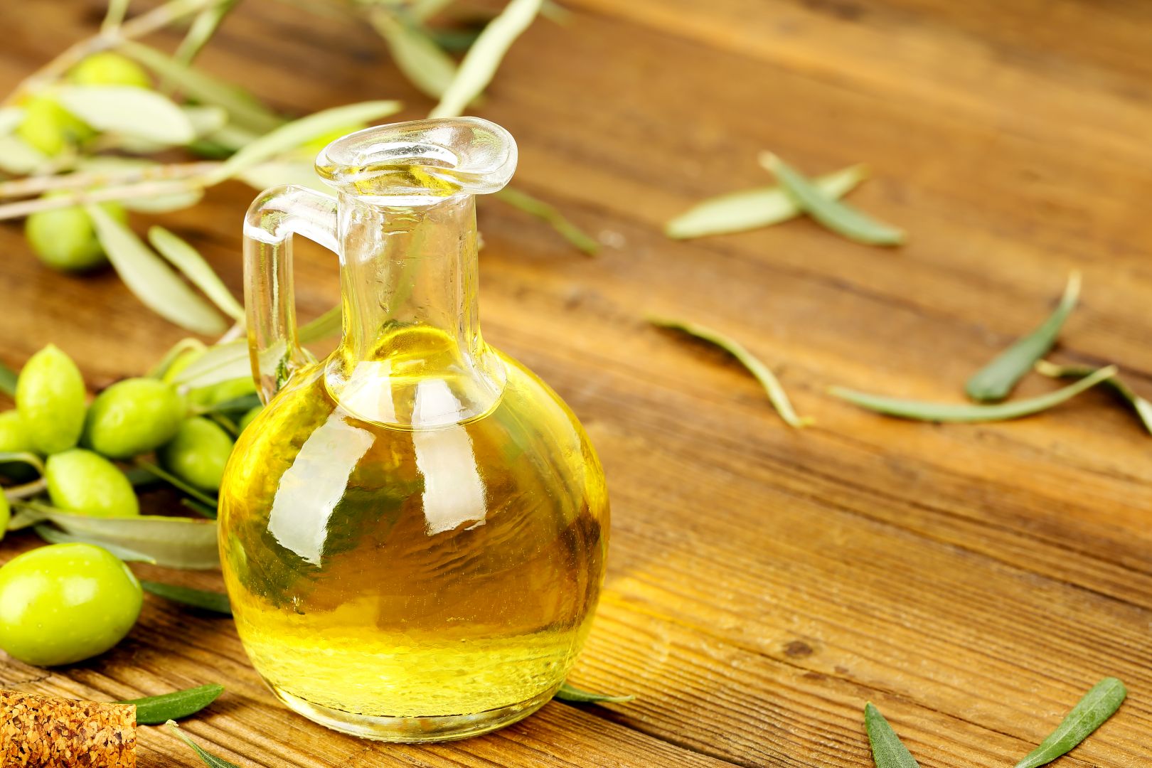 Olive oil jug with olive oil and olive tree branches on an old wooden table.